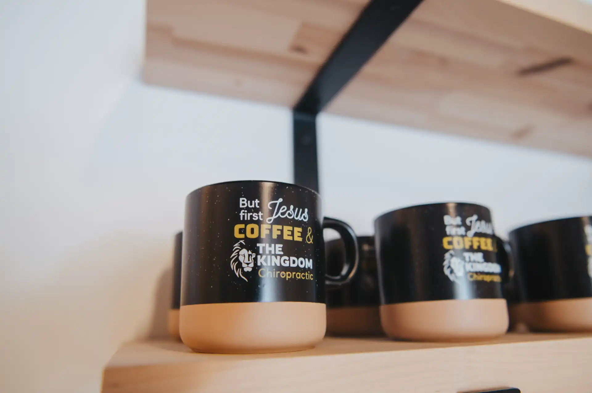 Branded "But first Jesus, Coffee & The Kingdom Chiropractic" mugs on a wooden shelf